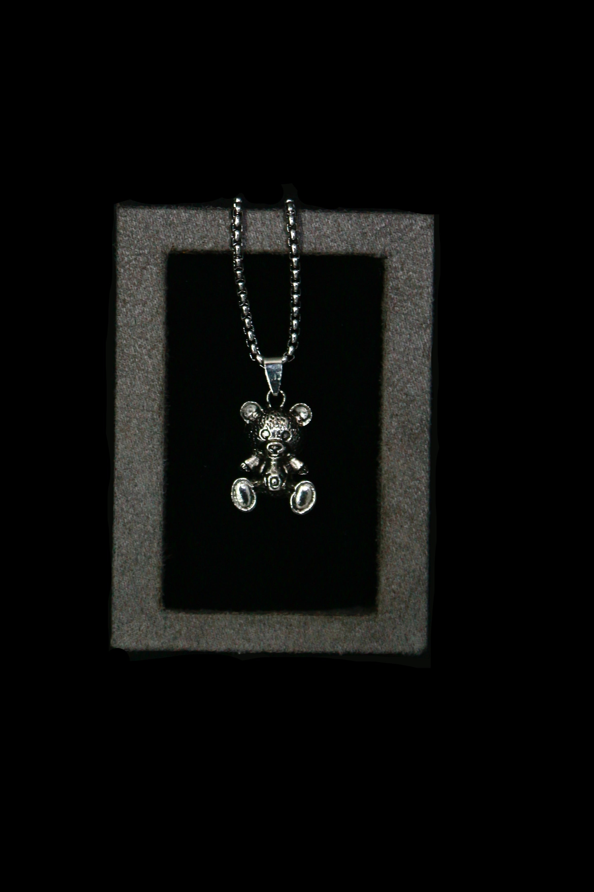 Silver teddy bear pendant necklace on a dark background